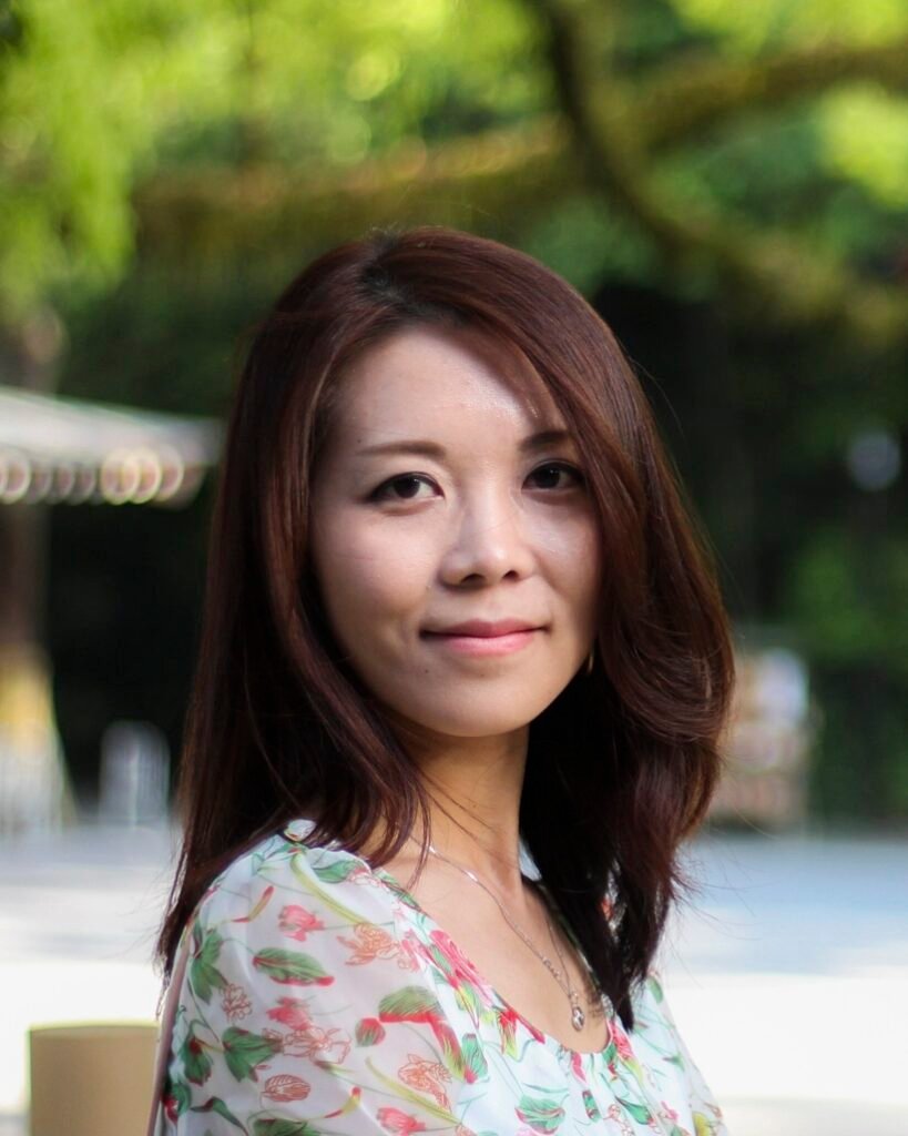A profile photo of Yuin in a soft colored floral dress on a blurred background of trees and ground